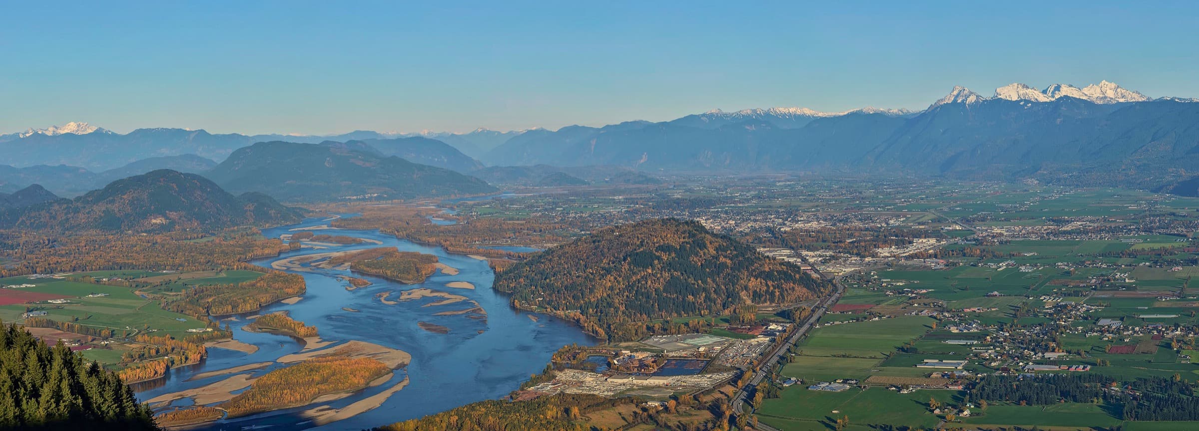 The Fraser River winding through Fraser Valley farmland with snow-capped mountains behind